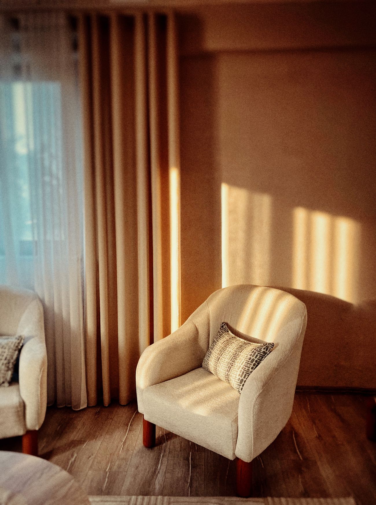 A cream armchair bathed in warm afternoon light through sheer curtains